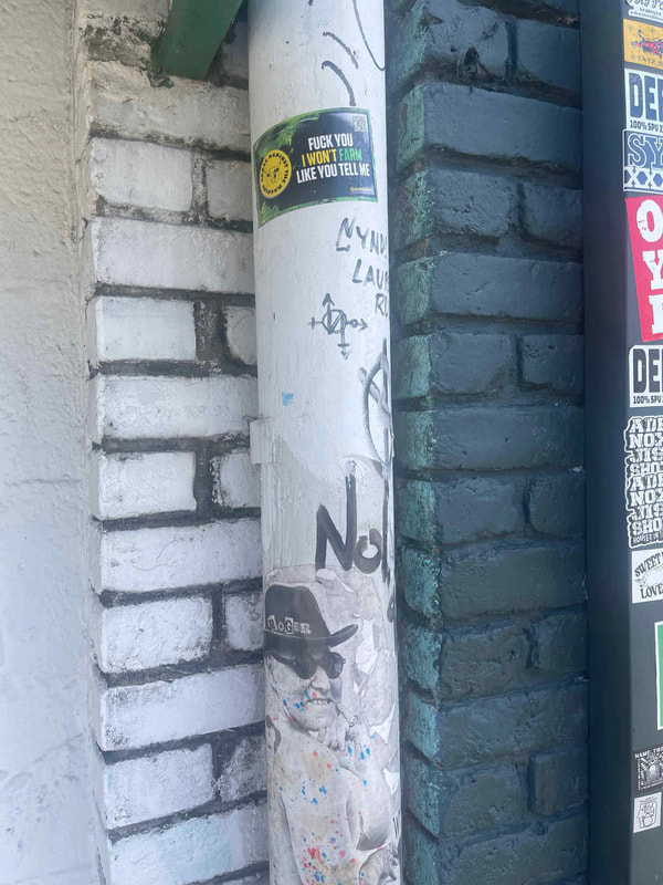 a white downpipe affixed with various stickers and other street art
