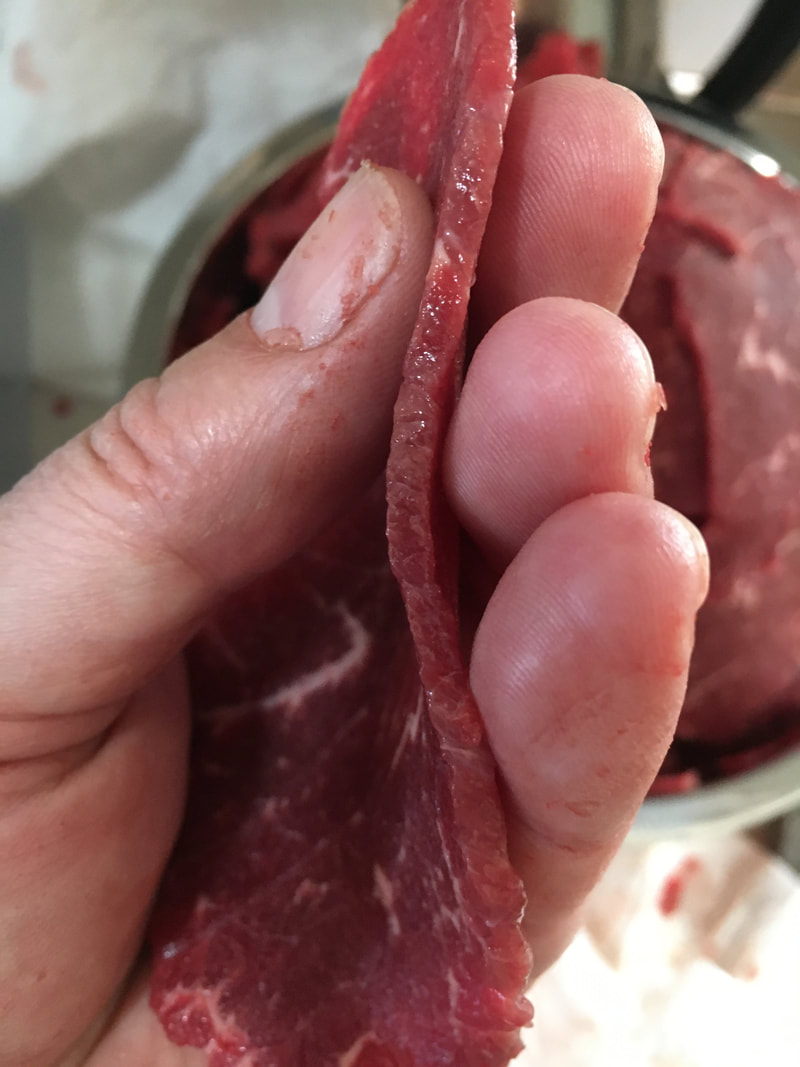 A hand showing the ideal tickness of Pineywoods beef cut for jerky