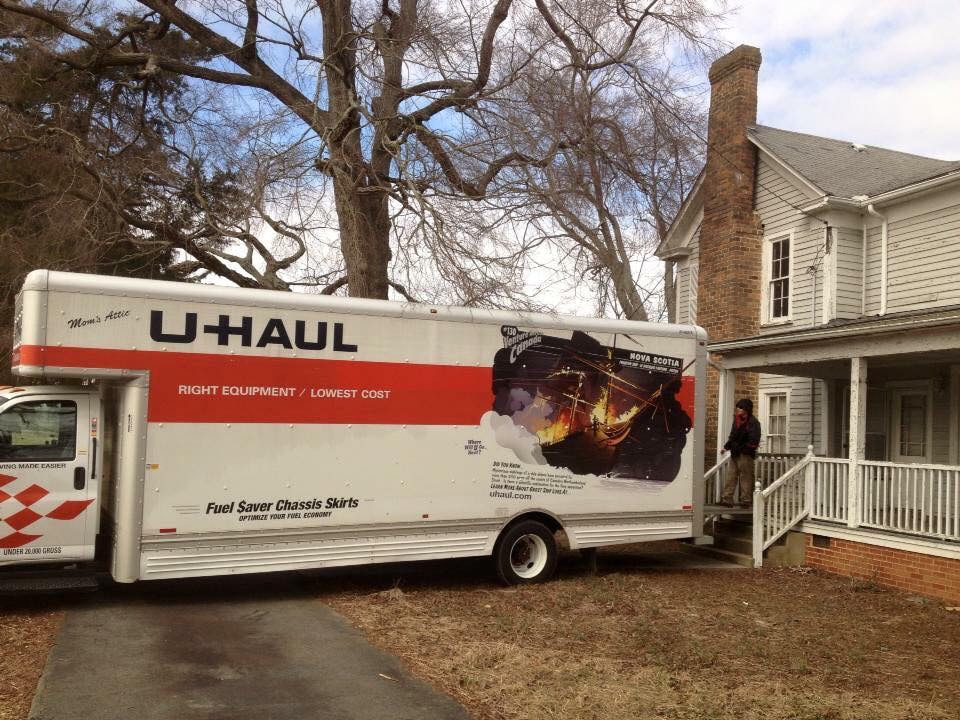 A Uhaul truck backed uo to the porch of an old grey farmhouse